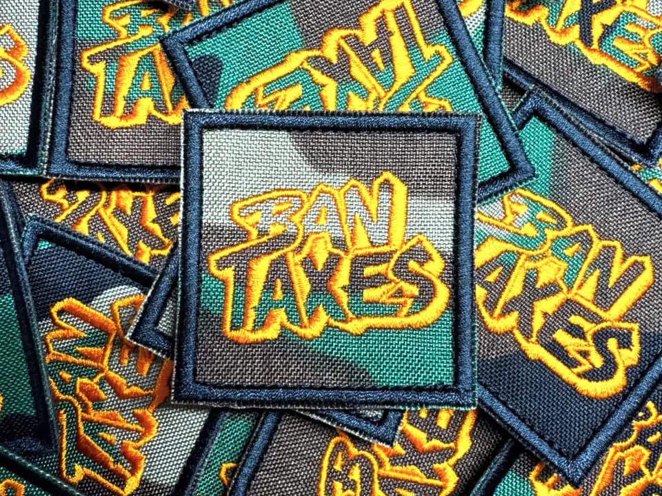 A pile of green and black Ban Taxes patches with orange embroidery