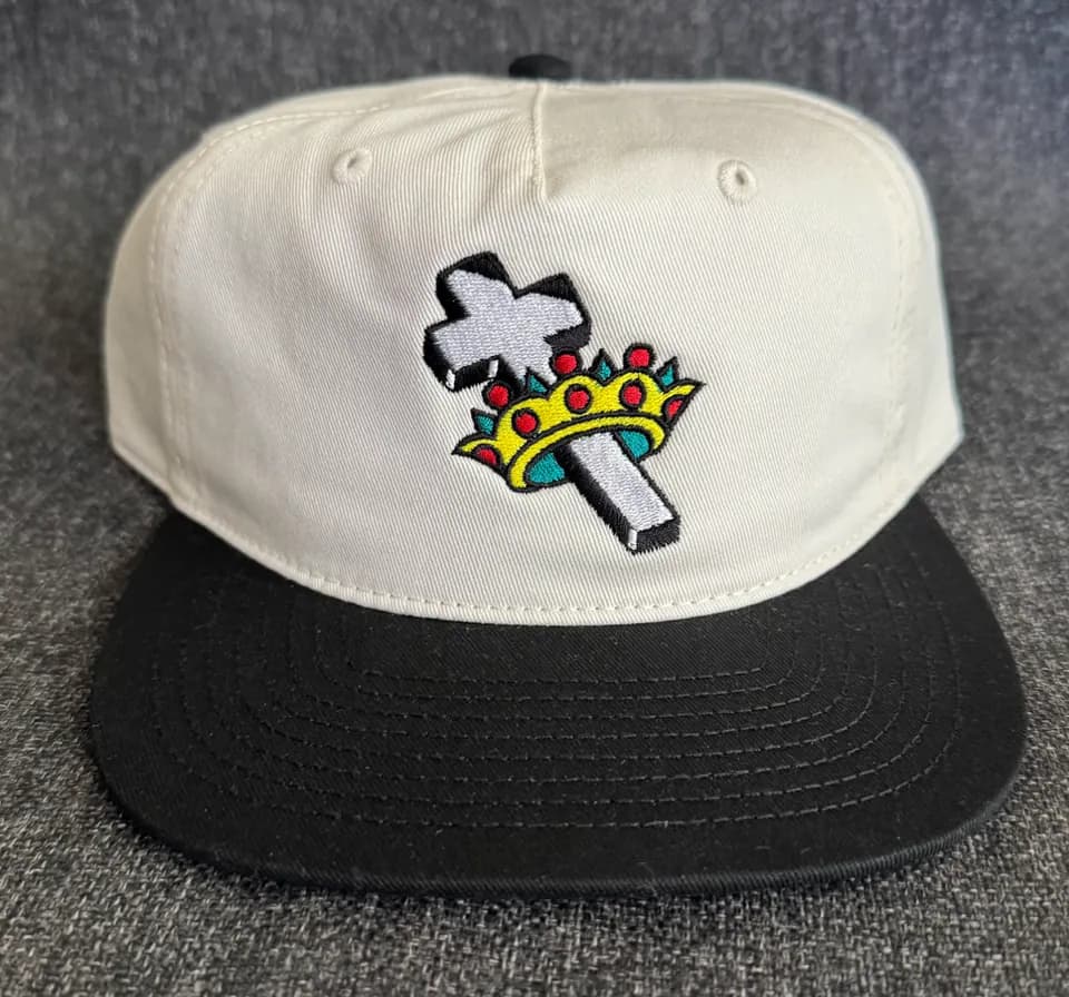A cream and black cap embroidered with a dagger and crown design