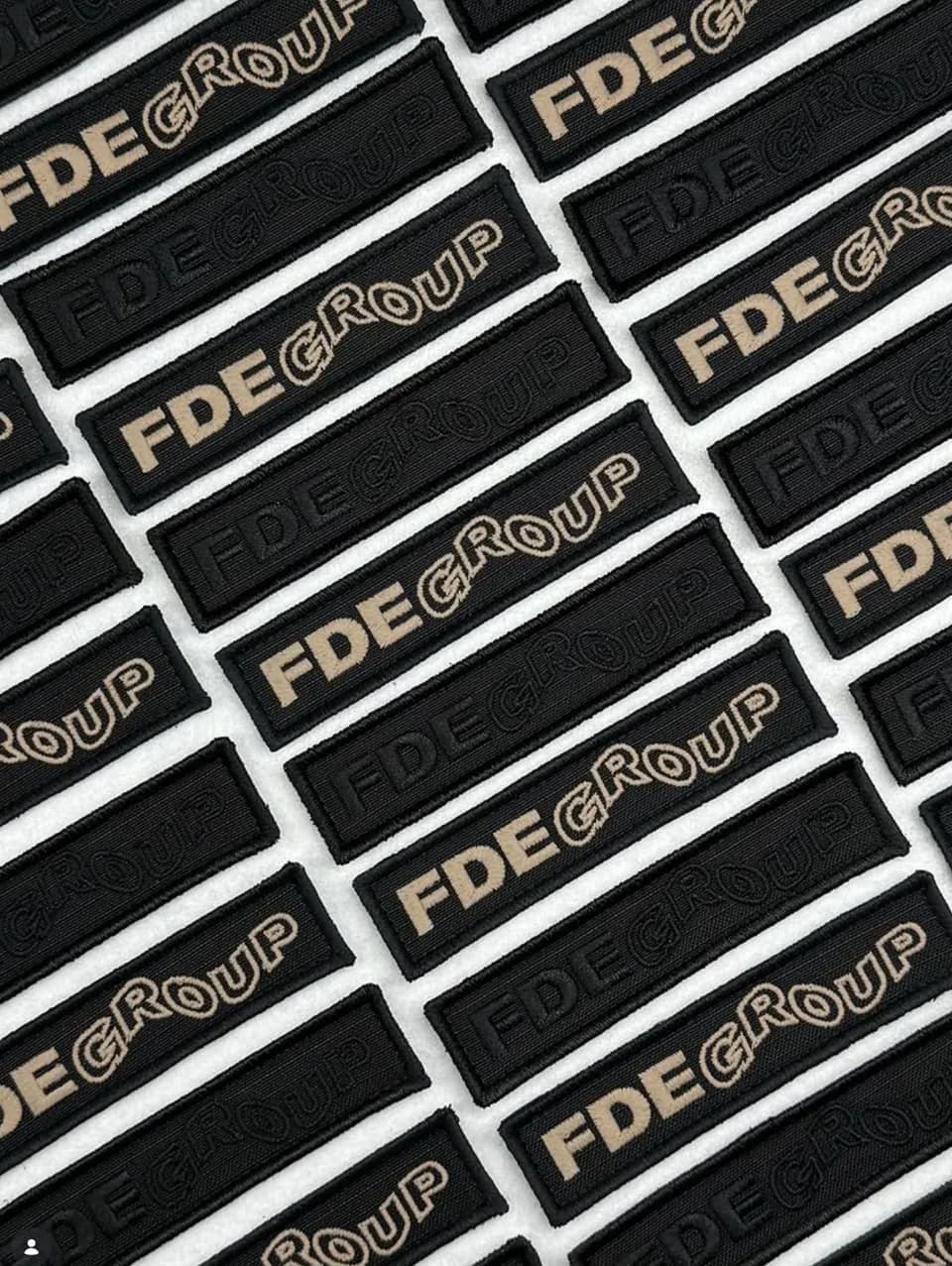 Rows of black FDE Group name patches embroidered in neutral colors