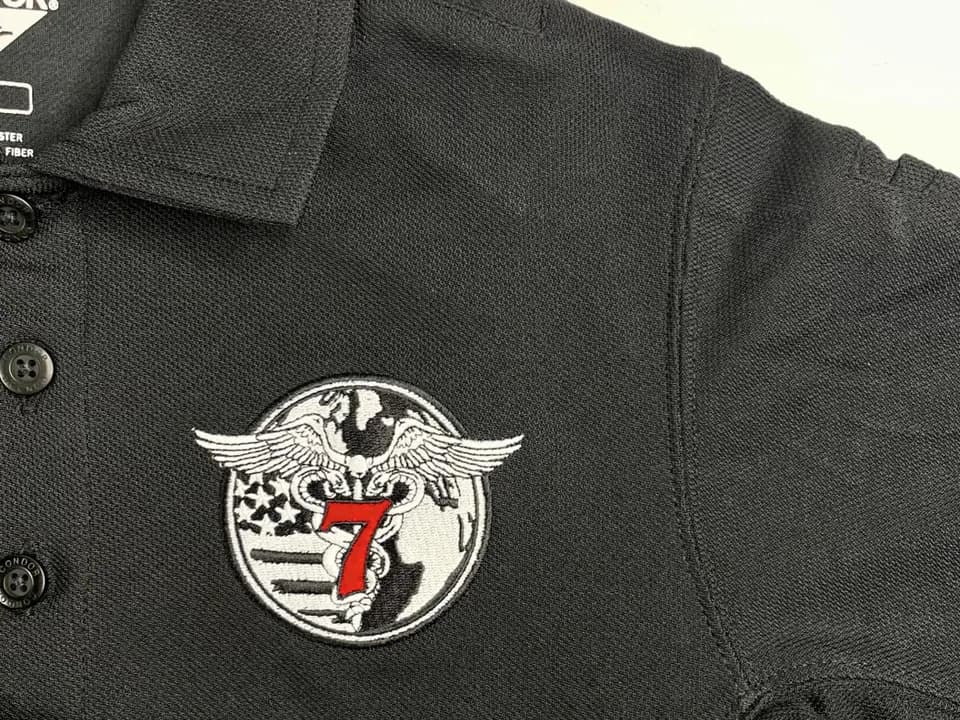 A black polo embroidered with a winged number seven emblem