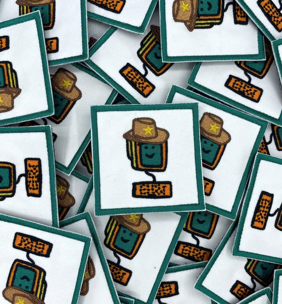 White Meme Projects patches embroidered with a green book character in a cowboy hat