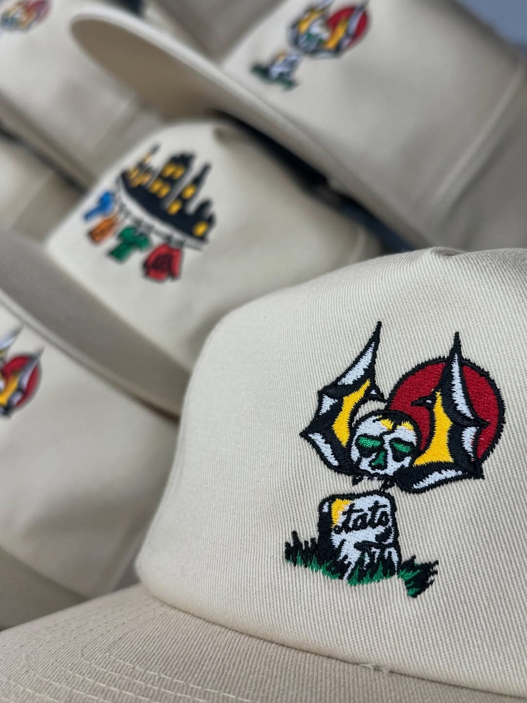 Cream caps embroidered with a colorful winged skull design