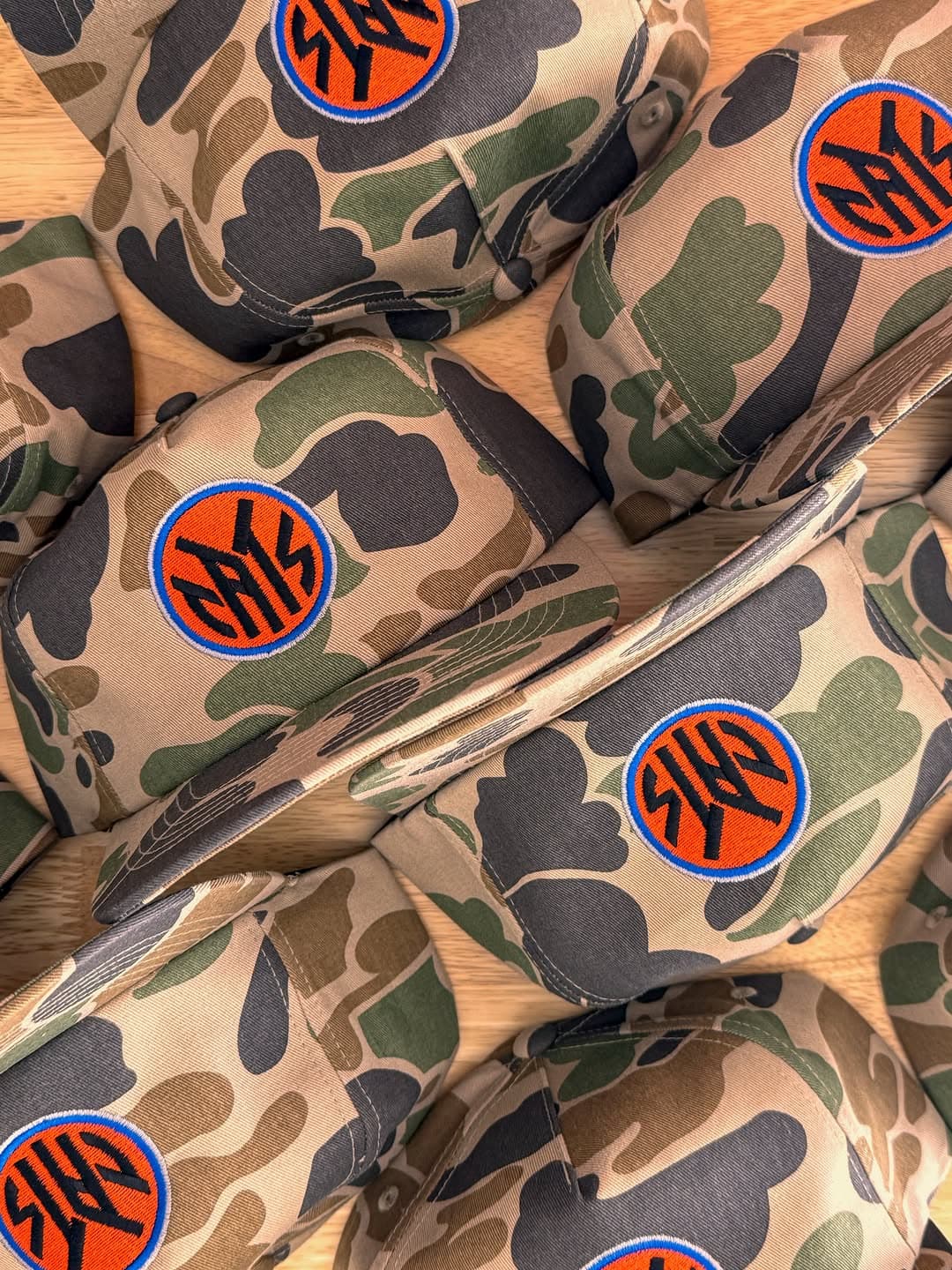 Camouflage caps embroidered with bright orange and navy circular monograms