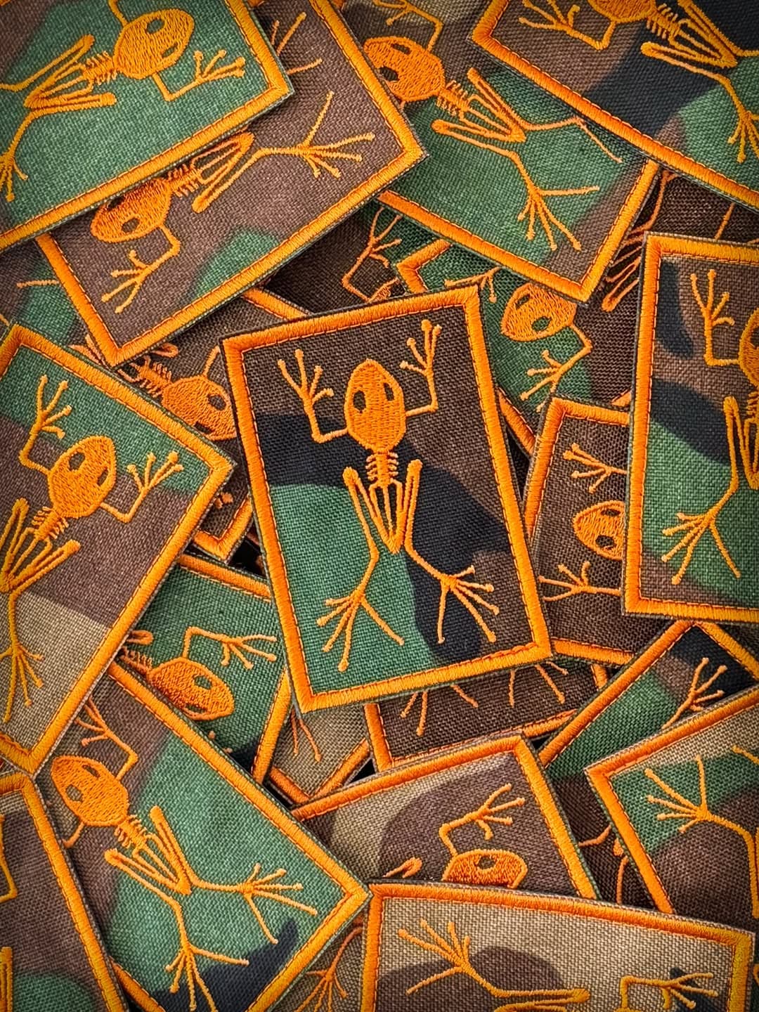Orange frog skeleton patches scattered across camouflage fabric