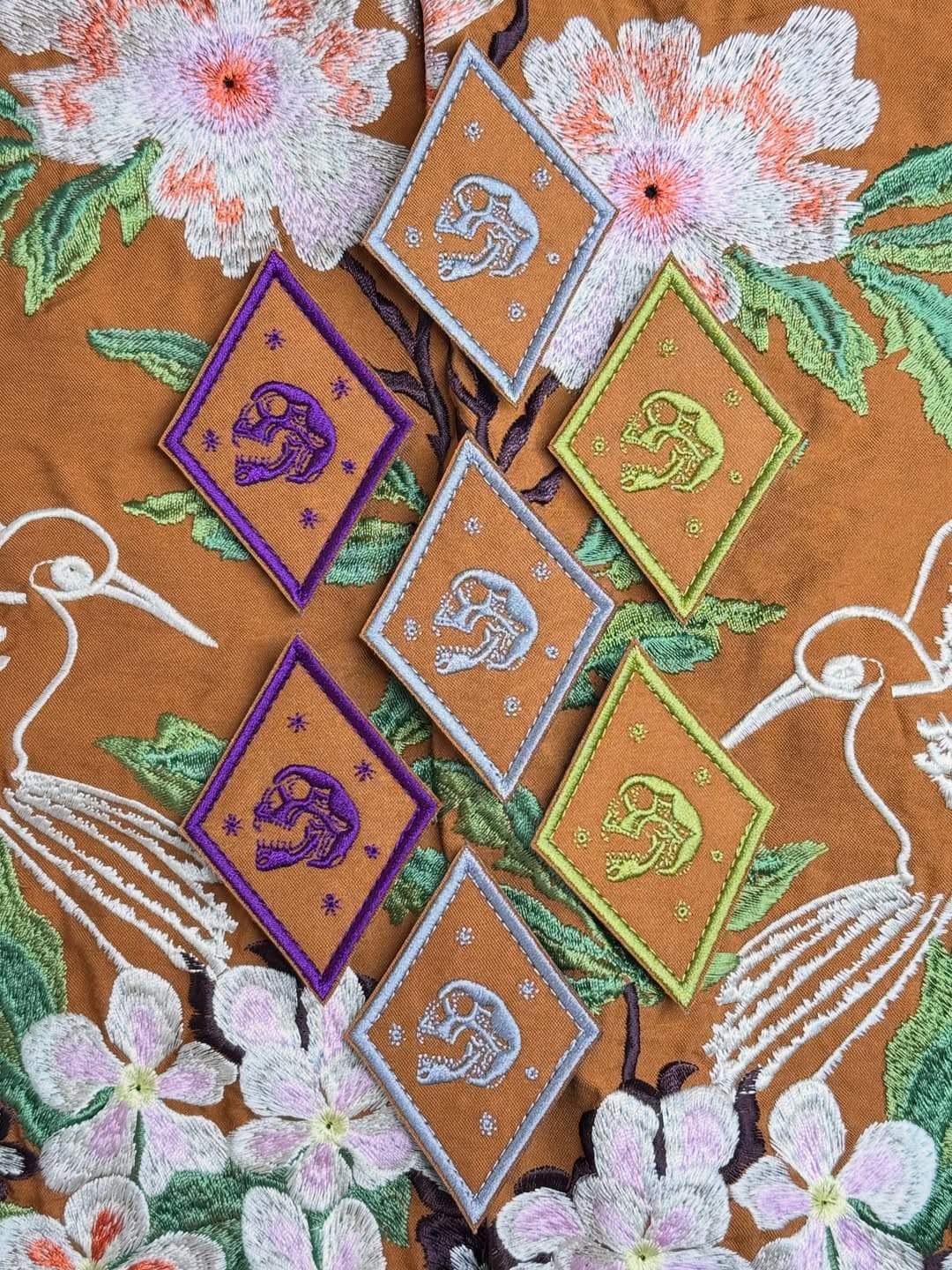 Diamond-shaped dinosaur skull patches arranged on embroidered floral fabric